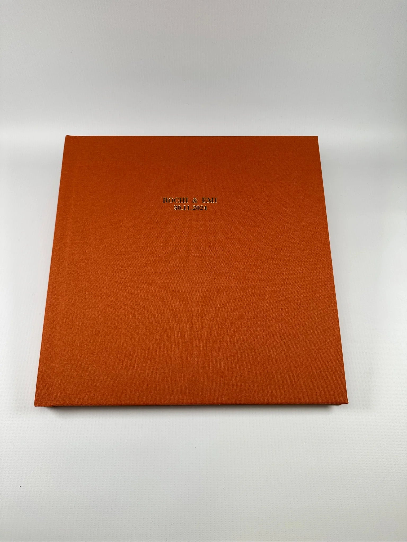 Fotolibro de boda con tapa de lino naranja terracota y personalización en hot stamping con los nombres de la pareja