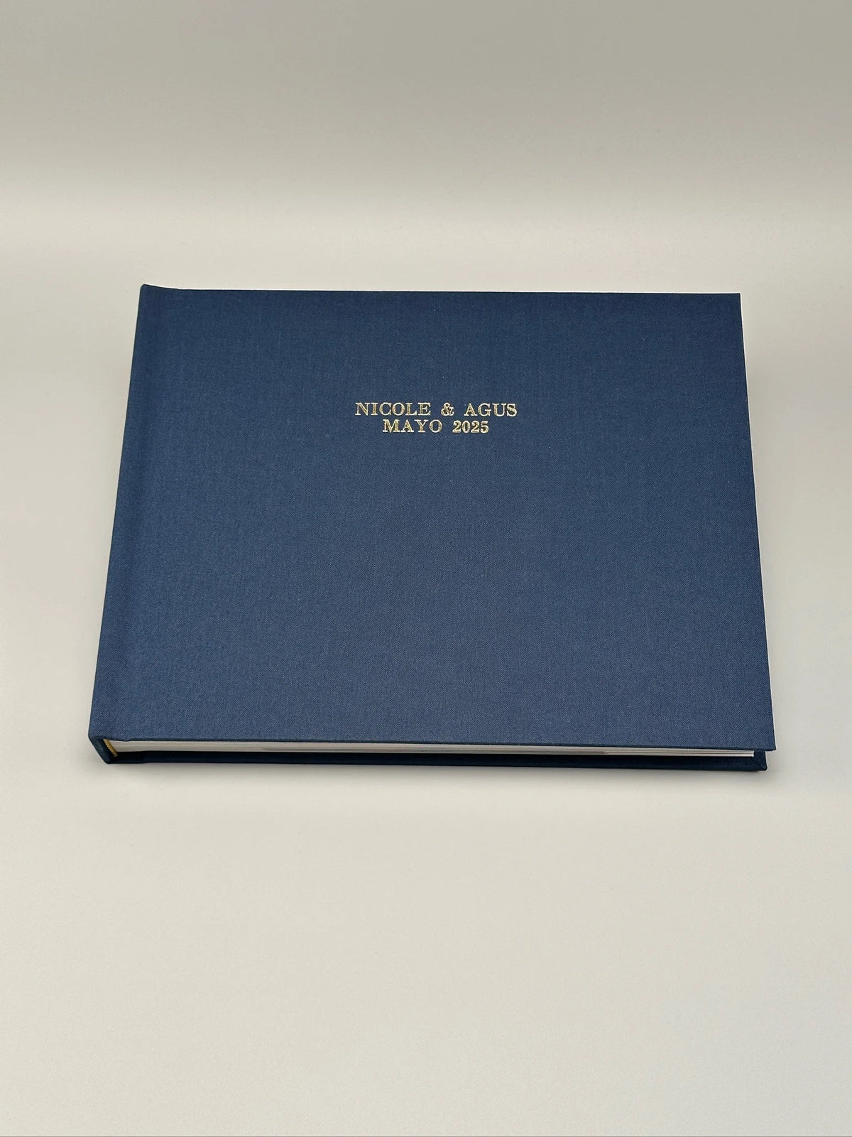 Fotolibro cerrado con tapa de lino azul marino y grabado dorado en hot stamping con los nombres de los novios y la fecha de la boda