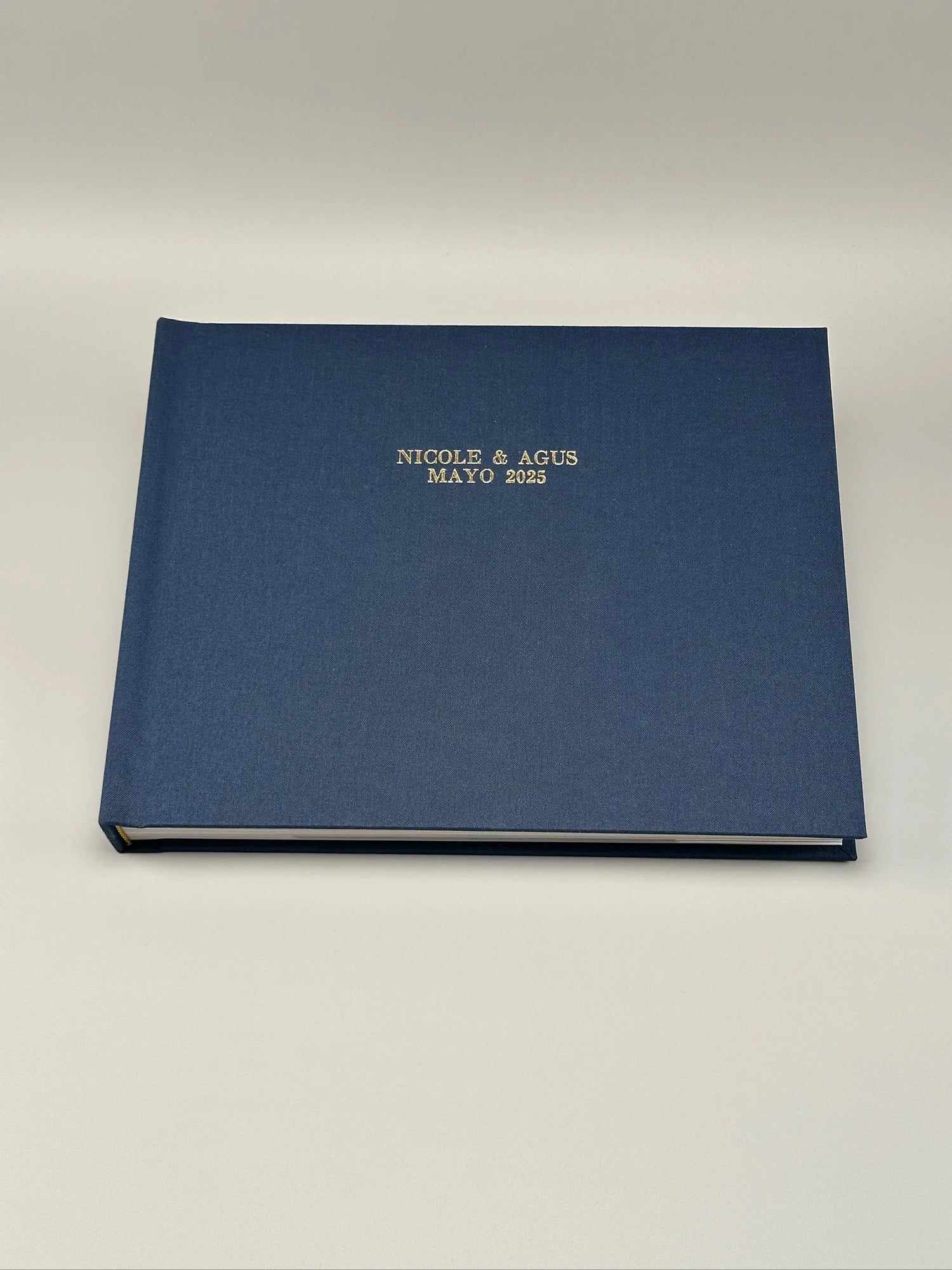 Fotolibro cerrado con tapa de lino azul marino y grabado dorado en hot stamping con los nombres de los novios y la fecha de la boda