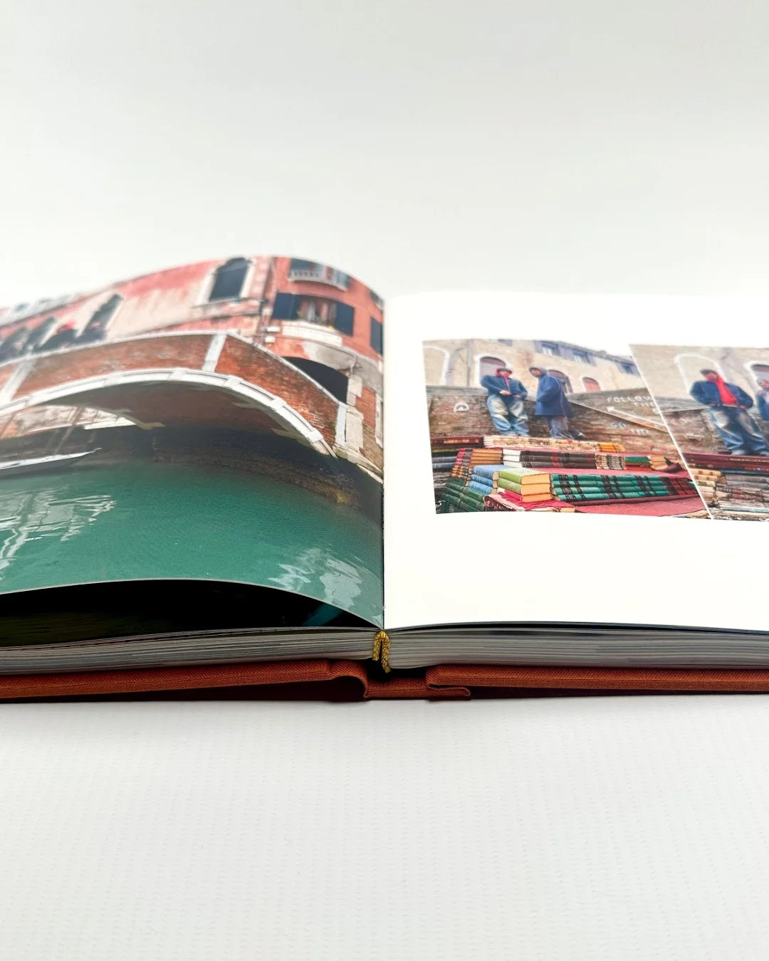 Álbum de viaje de tapa naranja abierto a doble página con fotos de Venecia y encuadernación cosida a mano visible en el lomo