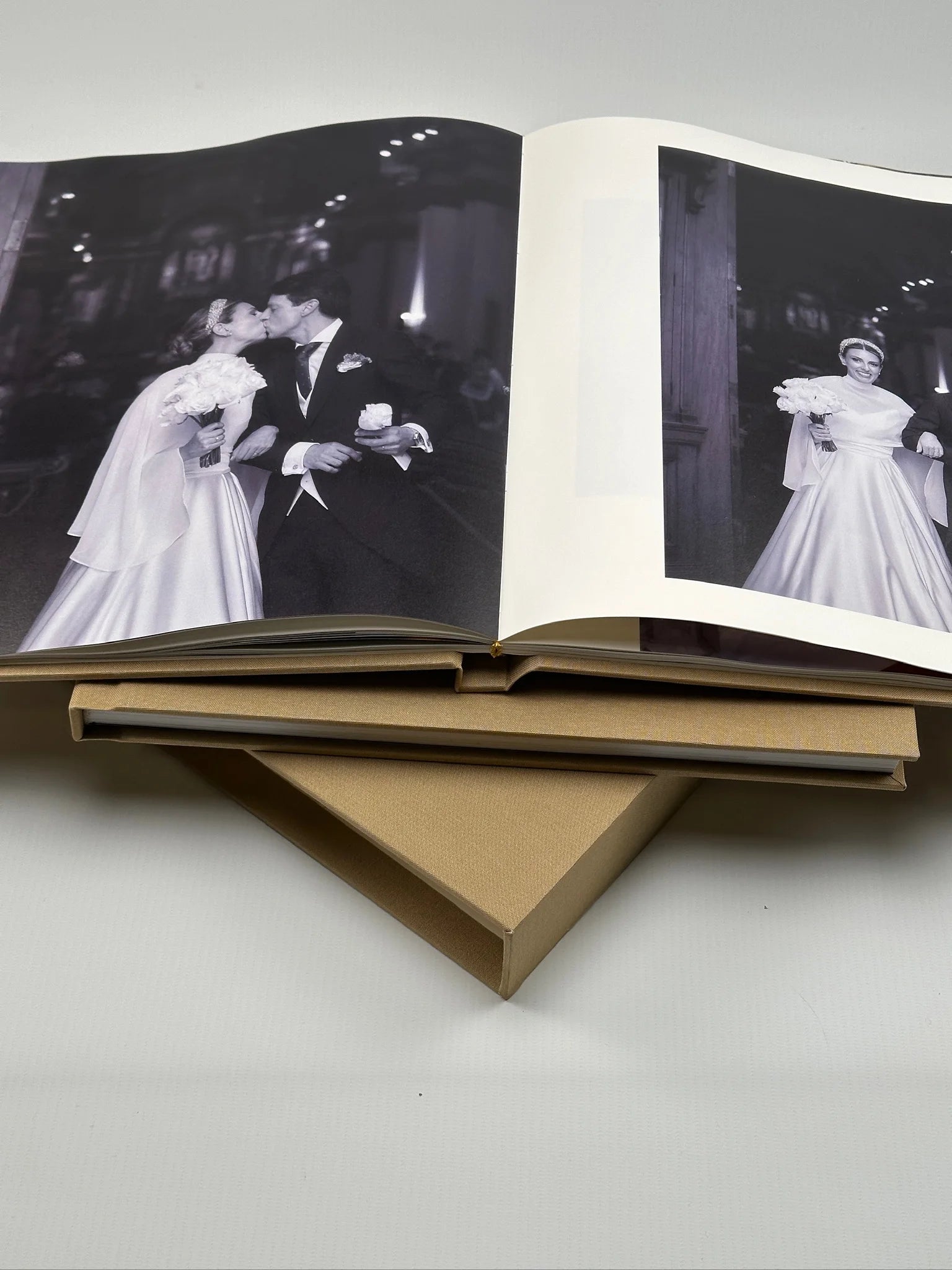 Dos fotolibros de tapa de lino beige, uno abierto a doble página con fotos de boda en blanco y negro
