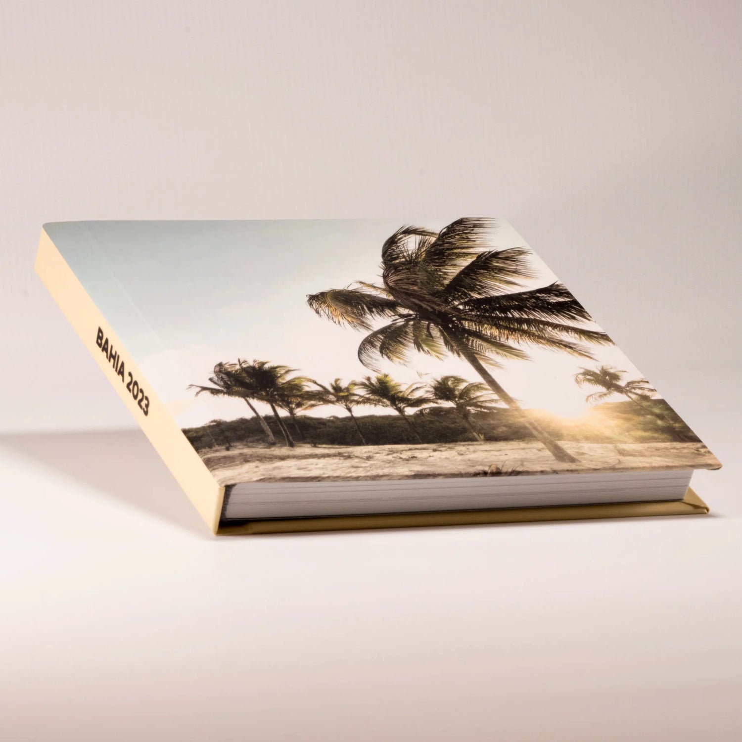 Fotolibro de viaje cerrado con tapa impresa de palmeras al atardecer, lomo personalizado Bahía 2023 y hojas rígidas
