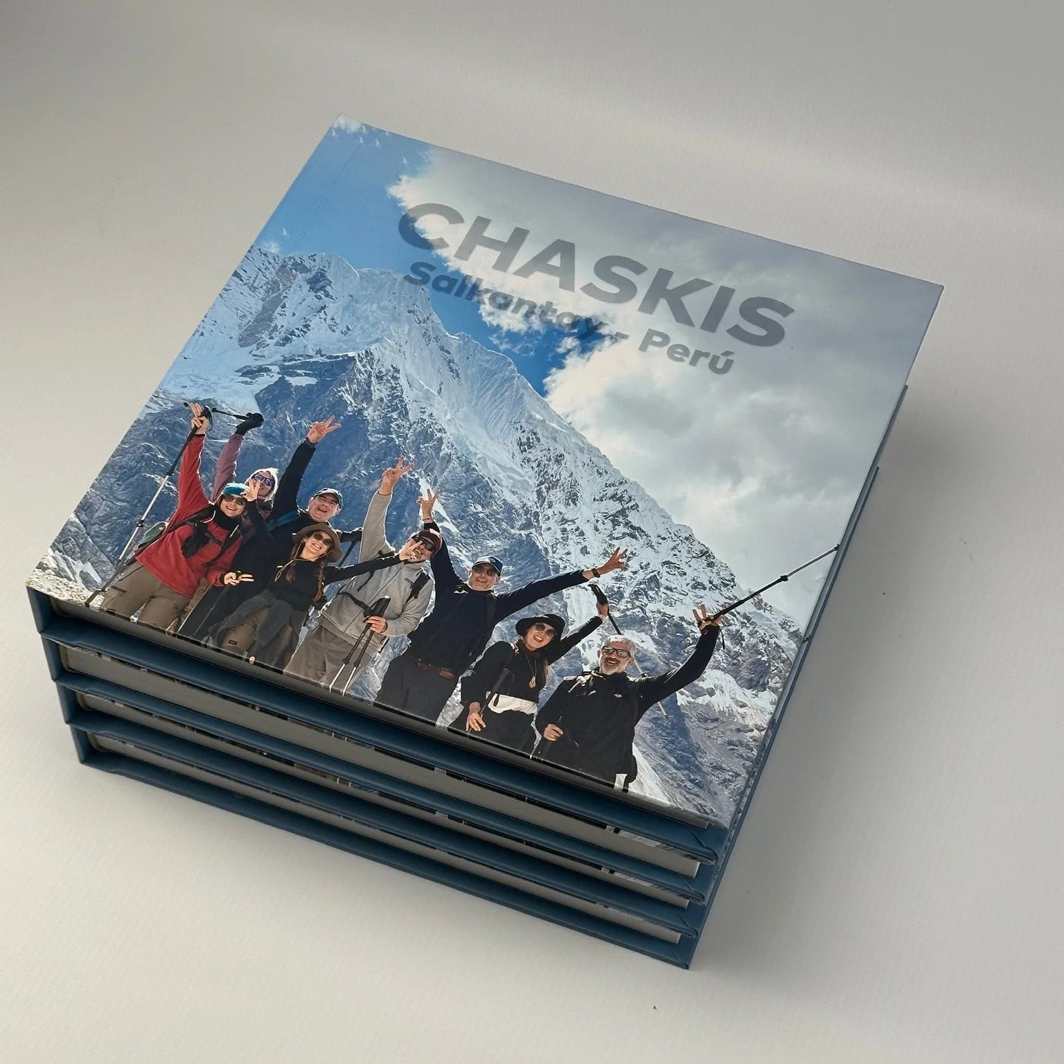 Pila de fotolibros con tapa impresa de un grupo de trekking frente a una montaña nevada, título Chaskis Salkantay Perú
