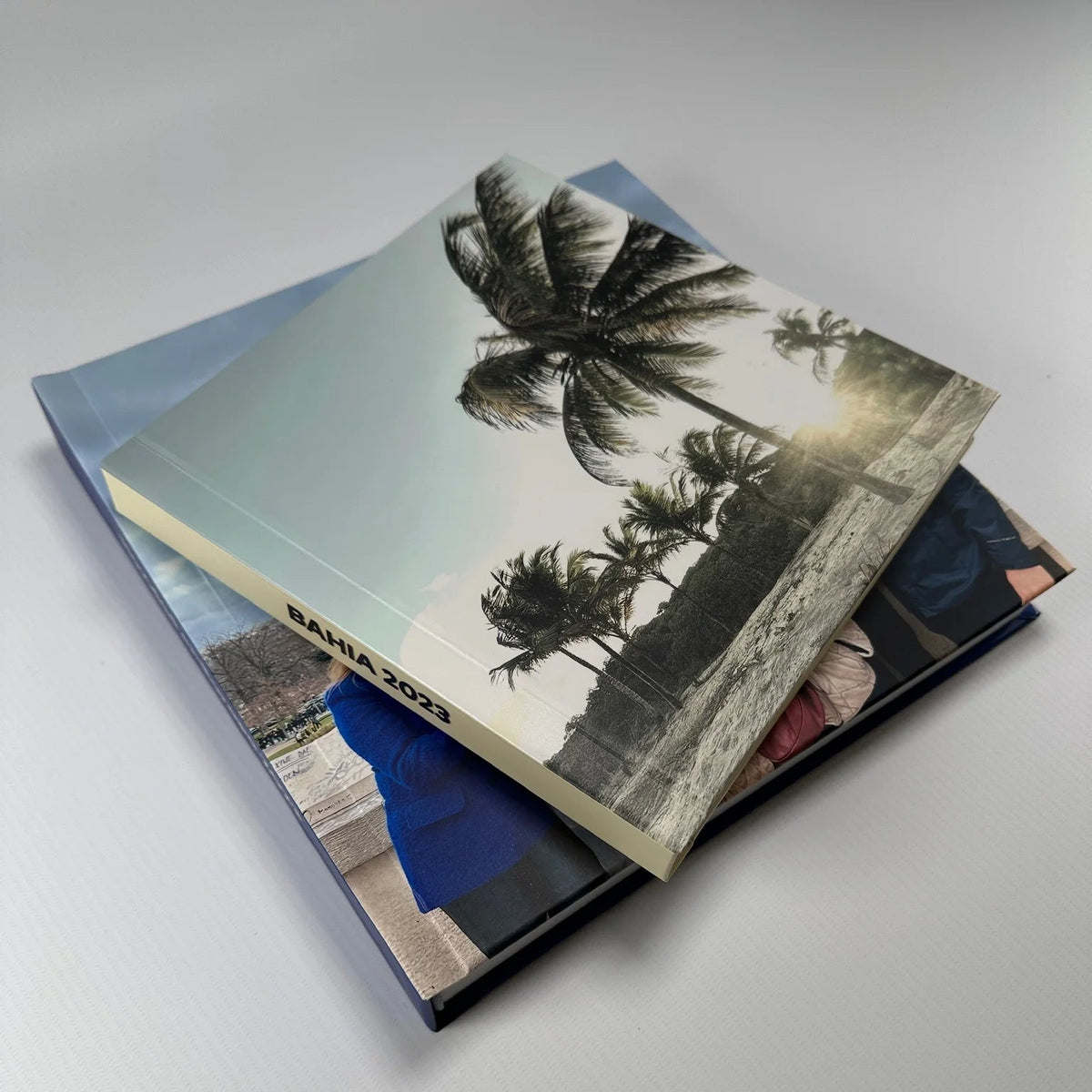 Dos fotolibros apilados con tapa fotográfica de playa y palmeras, mostrando el grosor y el acabado laminado mate