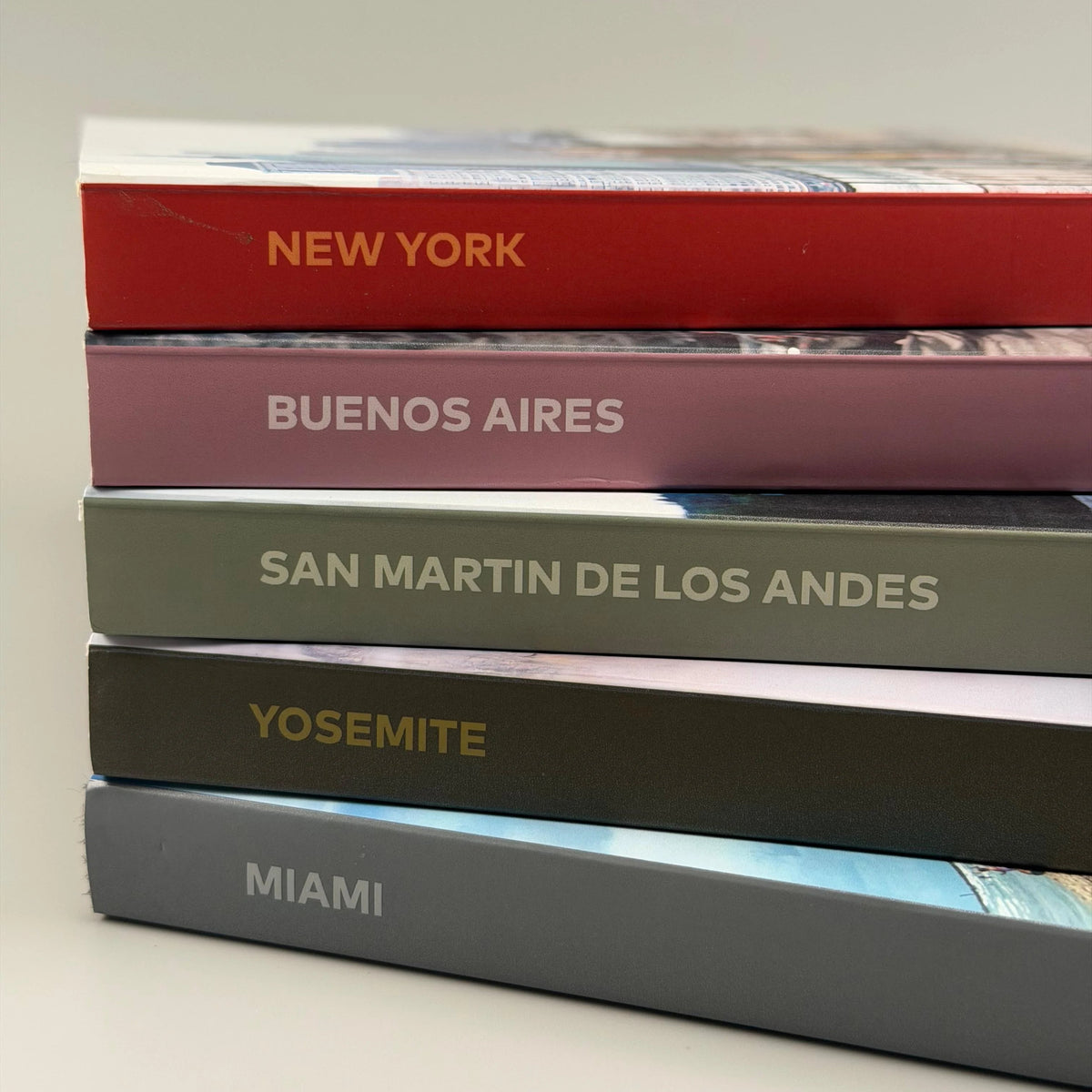 Pila de cinco fotolibros de viaje con lomos de colores y destinos como Nueva York, Buenos Aires y Yosemite