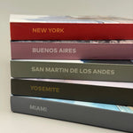 Pila de cinco fotolibros de viaje con lomos de colores y destinos como Nueva York, Buenos Aires y Yosemite