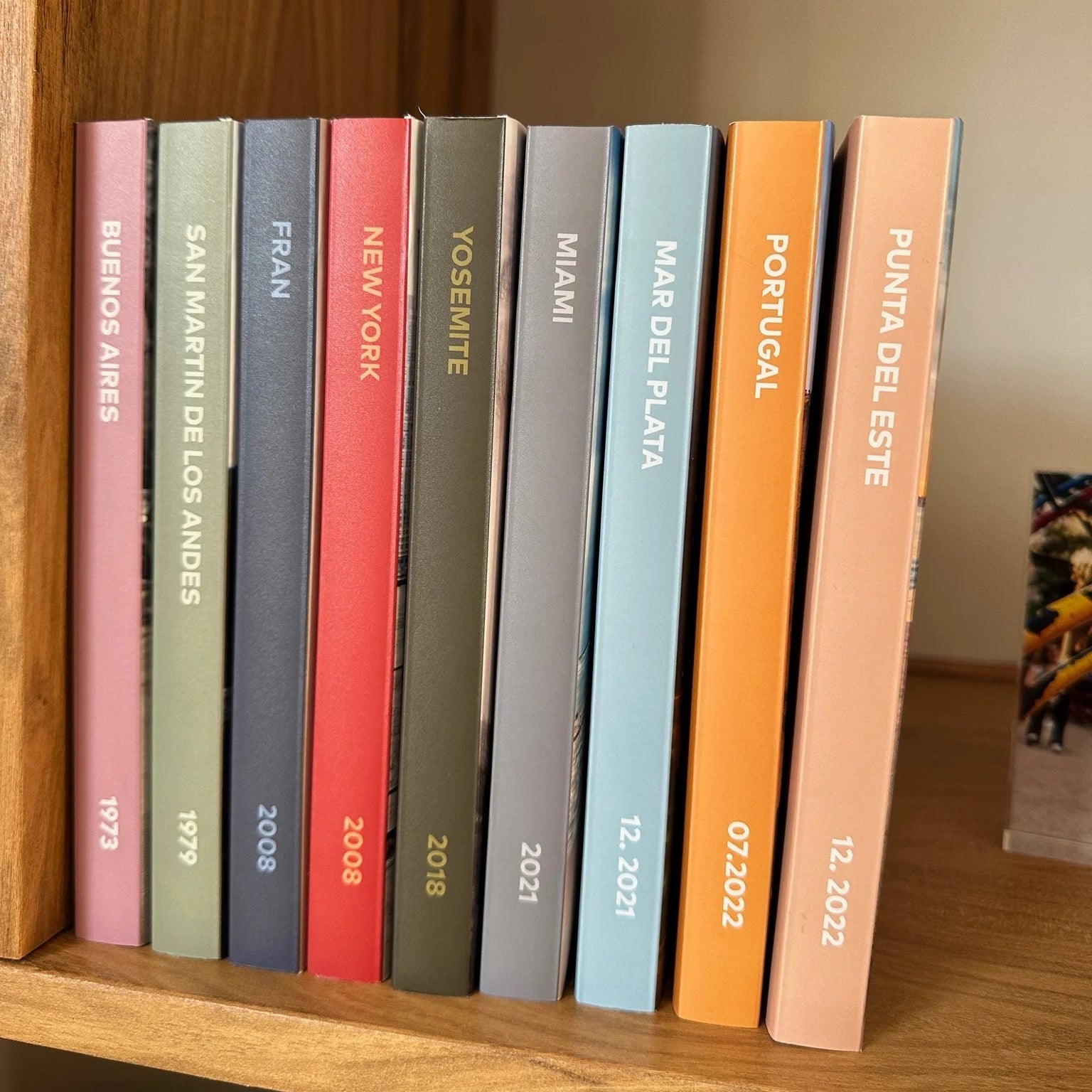 Colección de fotolibros parados en un estante de madera con lomos de colores y destinos de viaje
