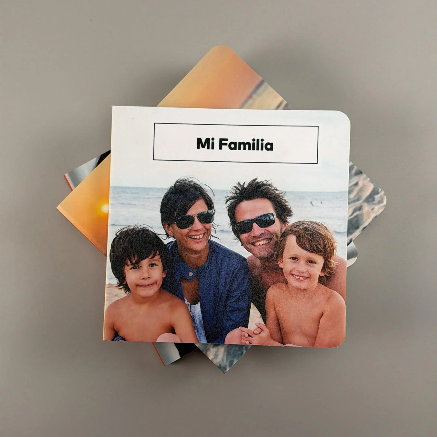 Fotolibro infantil de tapa rígida con foto familiar en la playa y el título Mi Familia, apoyado sobre otros libros