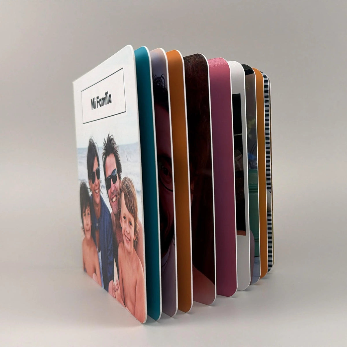 Fotolibro Mi Familia parado y abierto en abanico, dejando ver sus páginas rígidas de bordes coloridos y puntas redondeadas