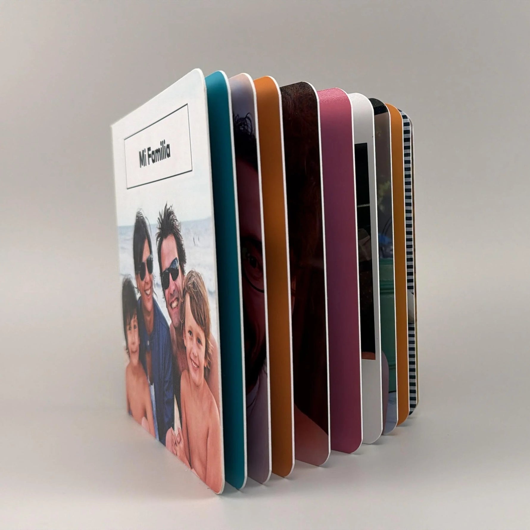Fotolibro Mi Familia parado y abierto en abanico, dejando ver sus páginas rígidas de bordes coloridos y puntas redondeadas