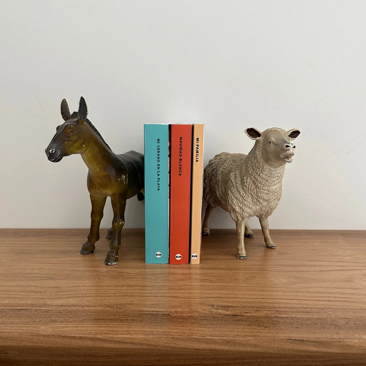Tres fotolibros infantiles parados entre sujetalibros con figuras de caballo y oveja sobre una repisa de madera