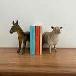 Tres fotolibros infantiles parados entre sujetalibros con figuras de caballo y oveja sobre una repisa de madera