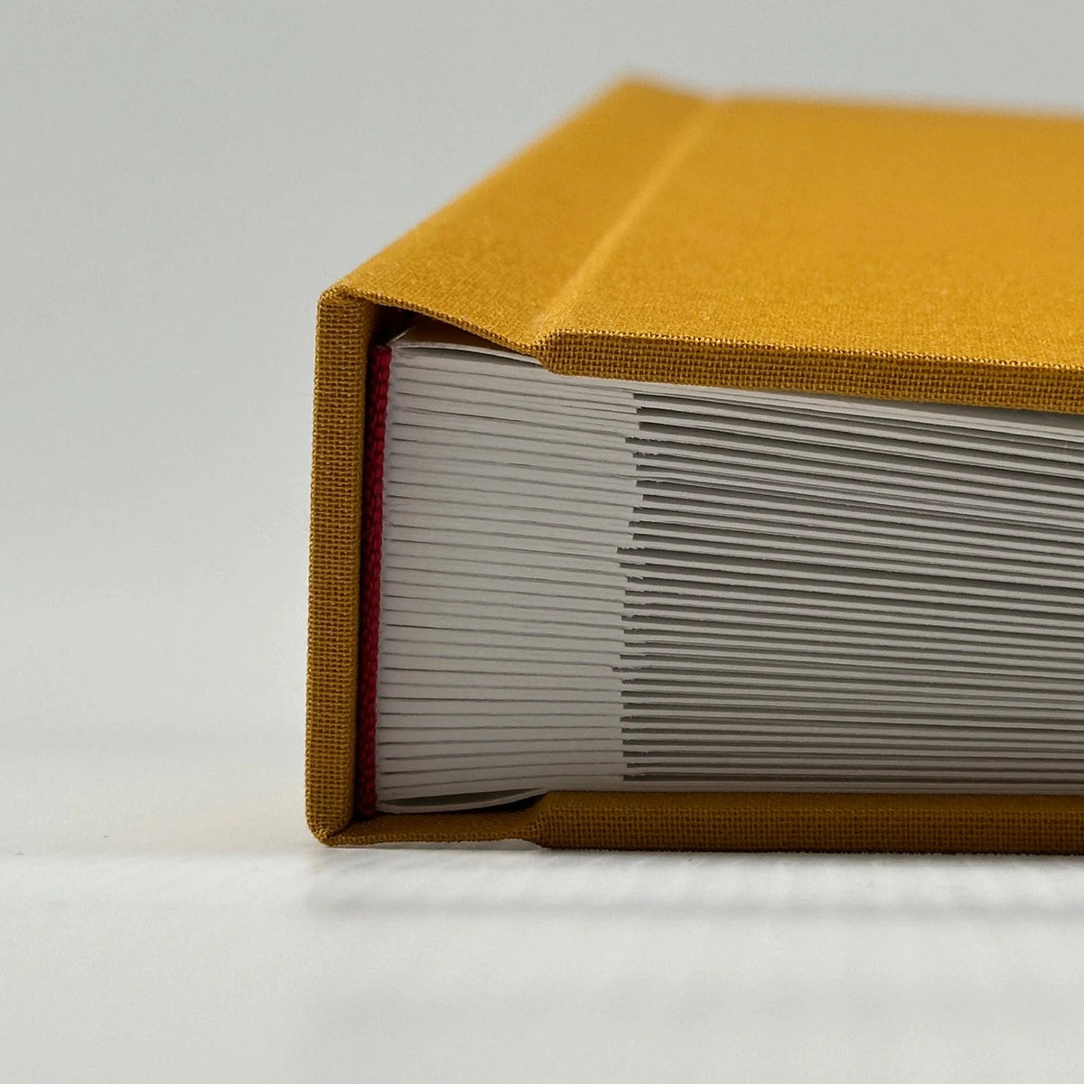 Detalle del canto y lomo de un álbum de lino amarillo mostrando las hojas gruesas y la cabezada roja