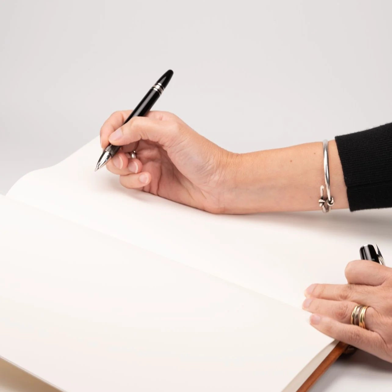 Persona escribiendo con lapicera negra sobre las páginas ahuesadas en blanco del libro de visitas abierto