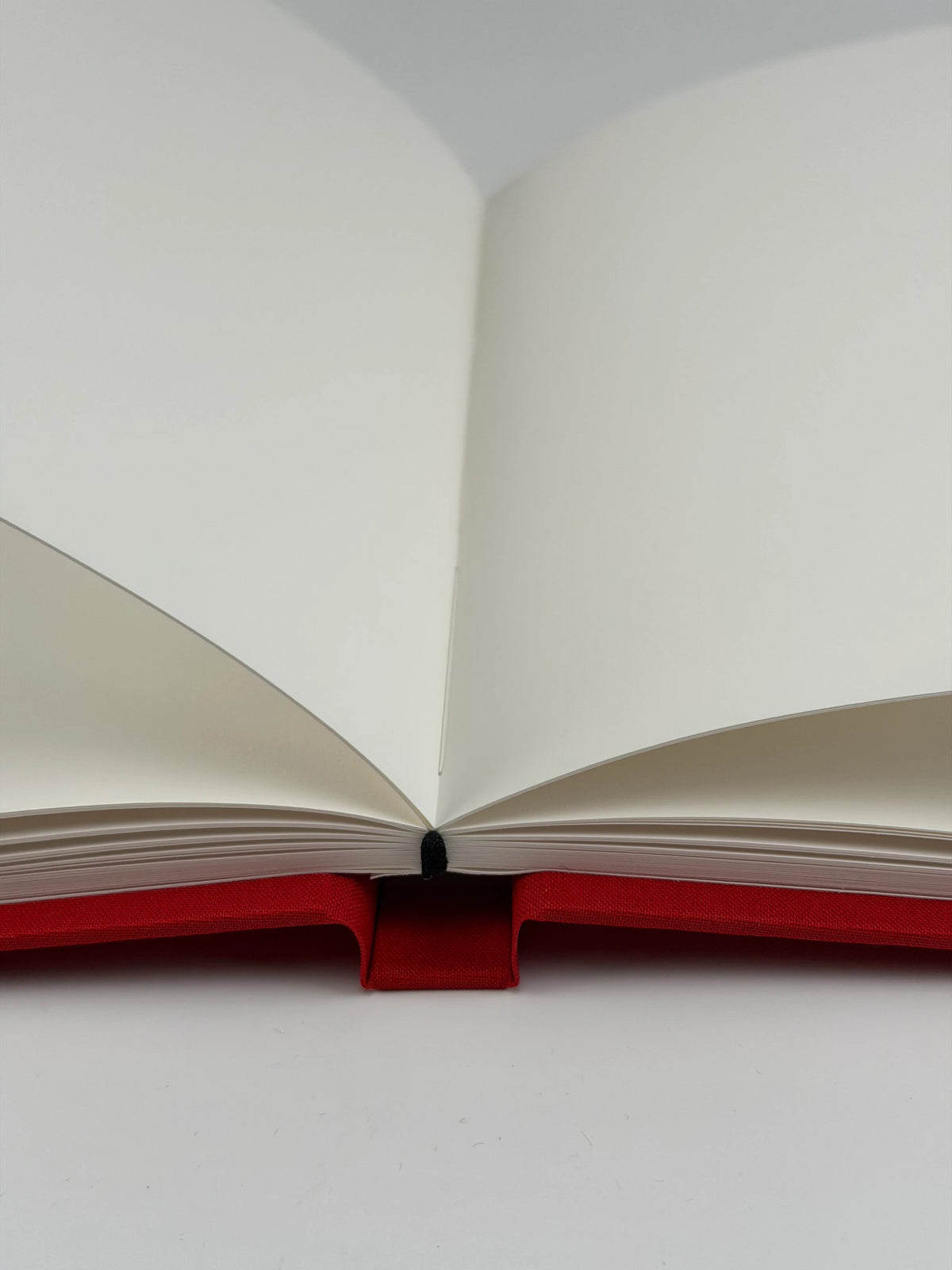 Cuaderno abierto a doble página mostrando el papel ahuesado texturado y la encuadernación cosida a mano sobre tapa de lino rojo