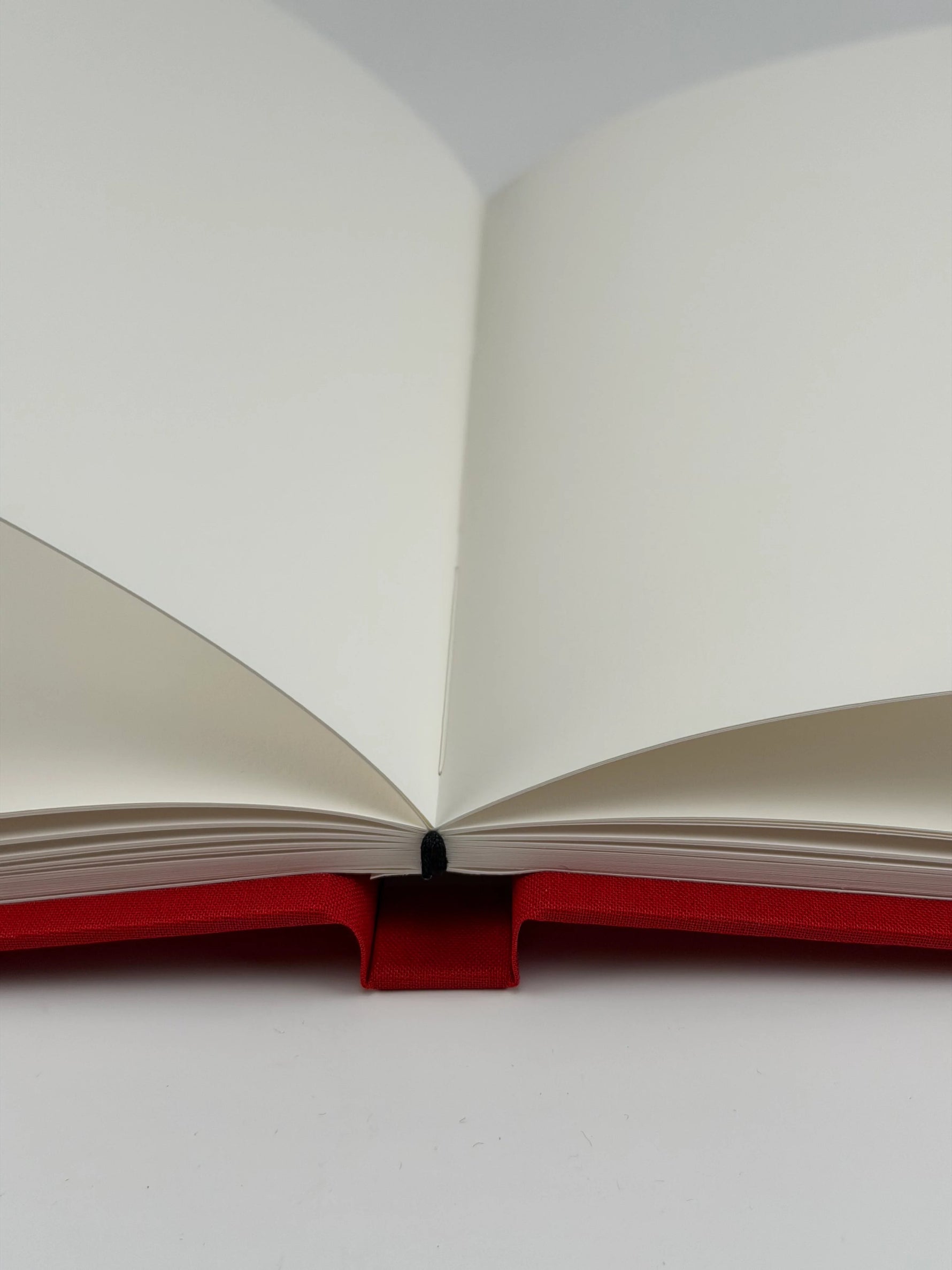 Cuaderno abierto a doble página mostrando el papel ahuesado texturado y la encuadernación cosida a mano sobre tapa de lino rojo