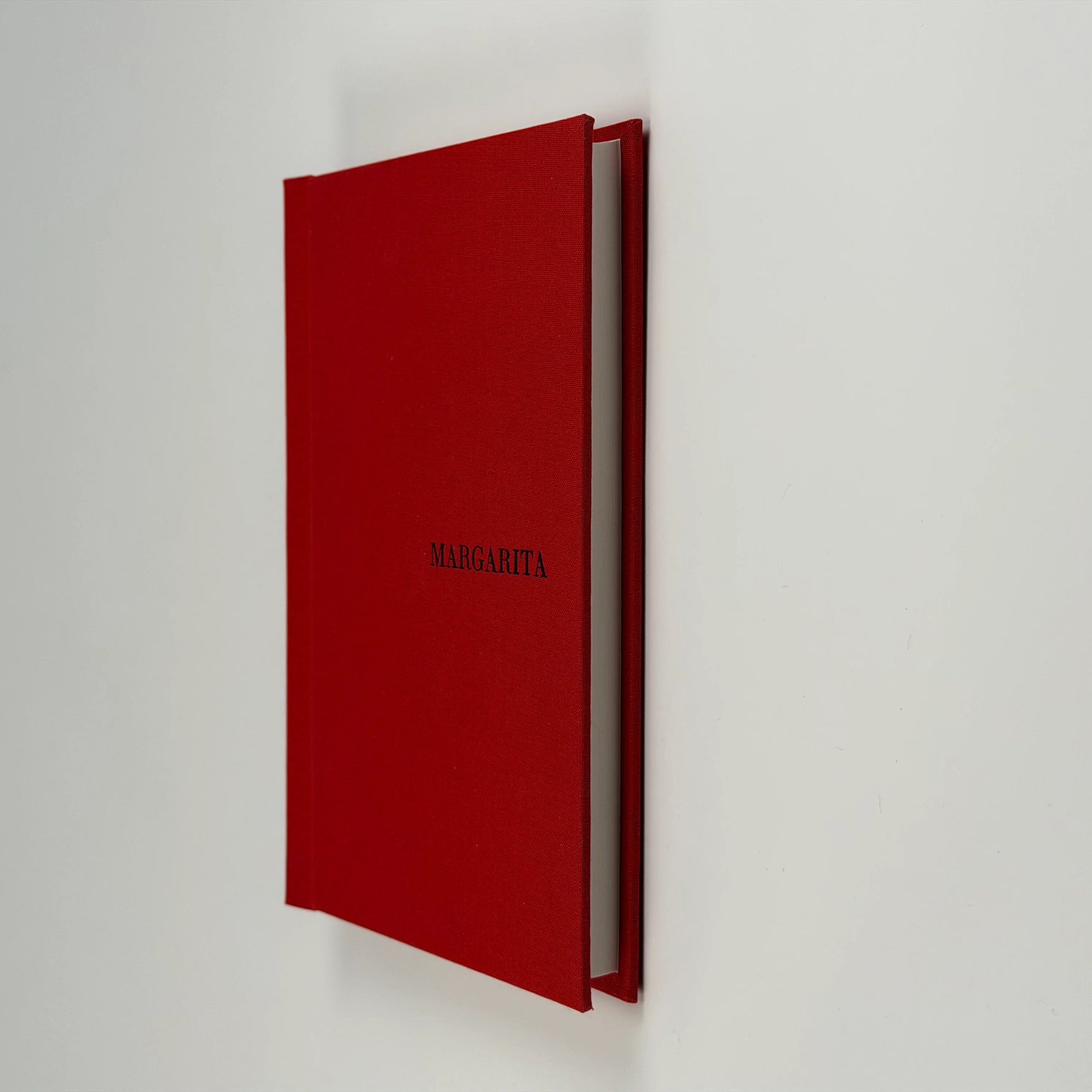 Cuaderno de tapa de lino rojo apoyado de canto y levemente abierto, con el nombre MARGARITA grabado en la tapa
