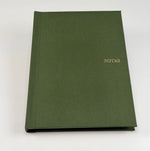 Cuaderno de tapa dura en lino verde oliva con la palabra NOTAS grabada en dorado por hot stamping