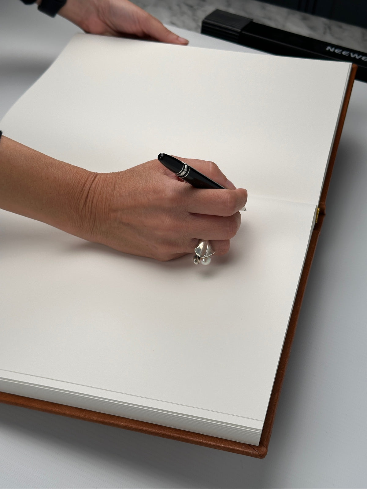 Persona escribiendo con lapicera sobre las hojas blancas de un libro de firmas abierto con tapa de cuero caramelo