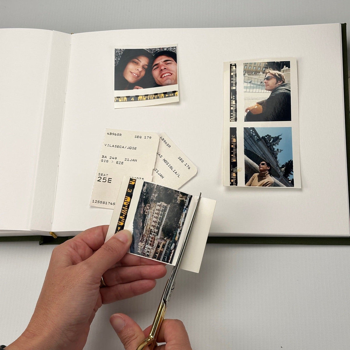 Álbum abierto con fotos de viaje y tickets de avión pegados; una mano recorta una foto con tijera