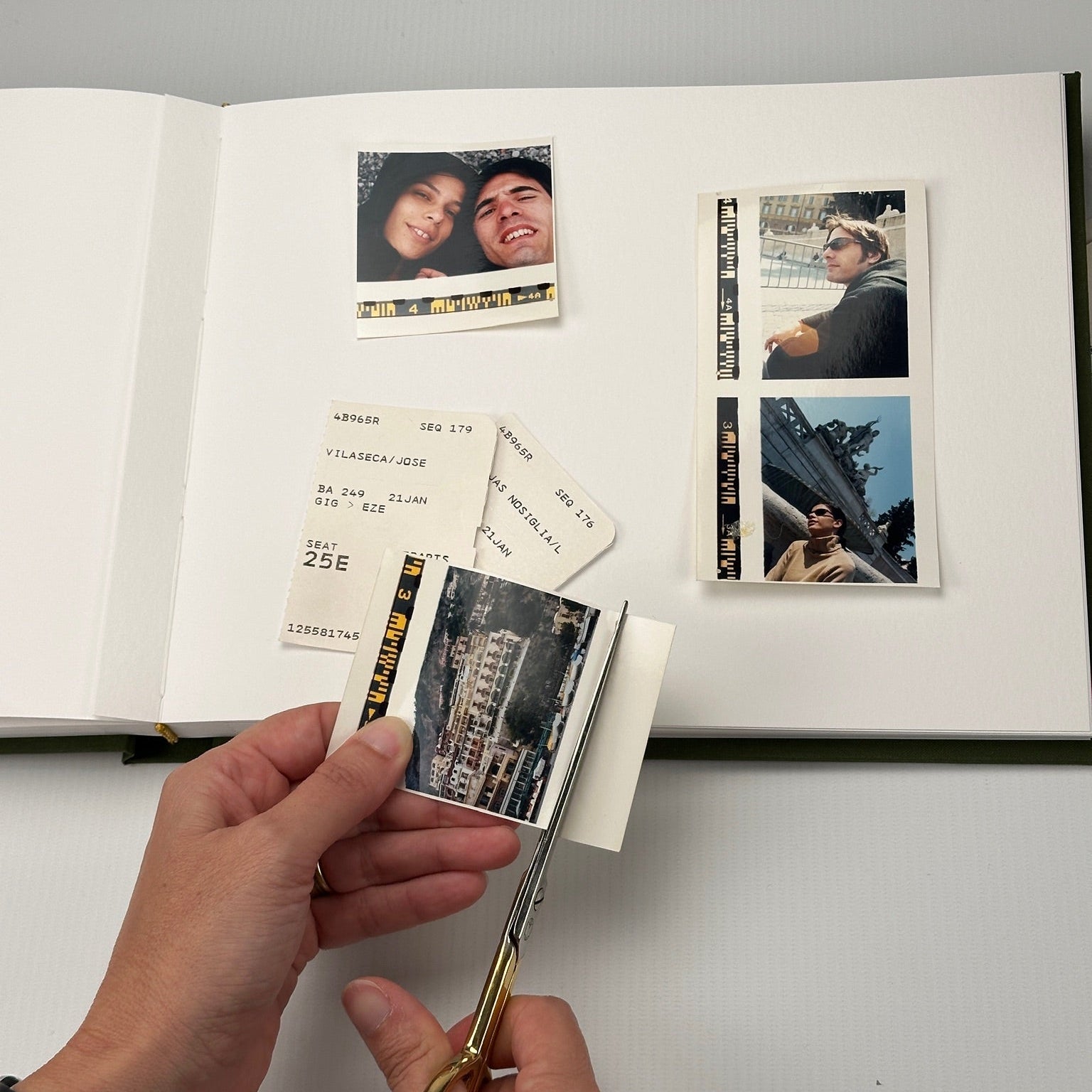 Álbum abierto con fotos de viaje y tickets de avión pegados; una mano recorta una foto con tijera