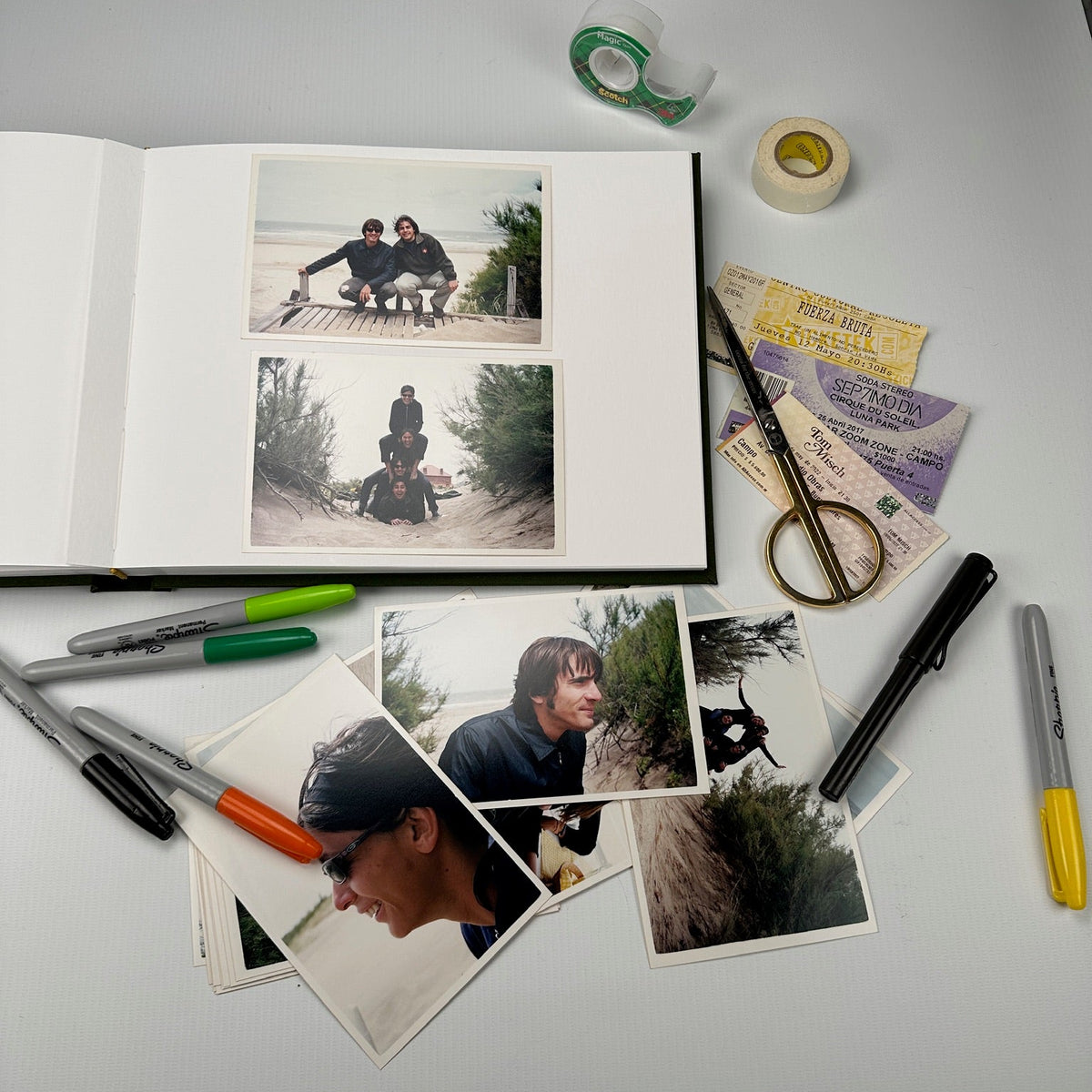 Álbum abierto sobre la mesa con fotos de playa pegadas, fibrones, tijera y entradas de show listas para armar