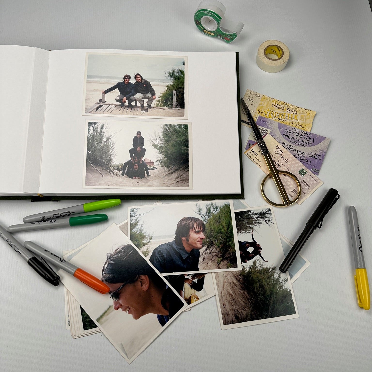 Álbum abierto sobre la mesa con fotos de playa pegadas, fibrones, tijera y entradas de show listas para armar
