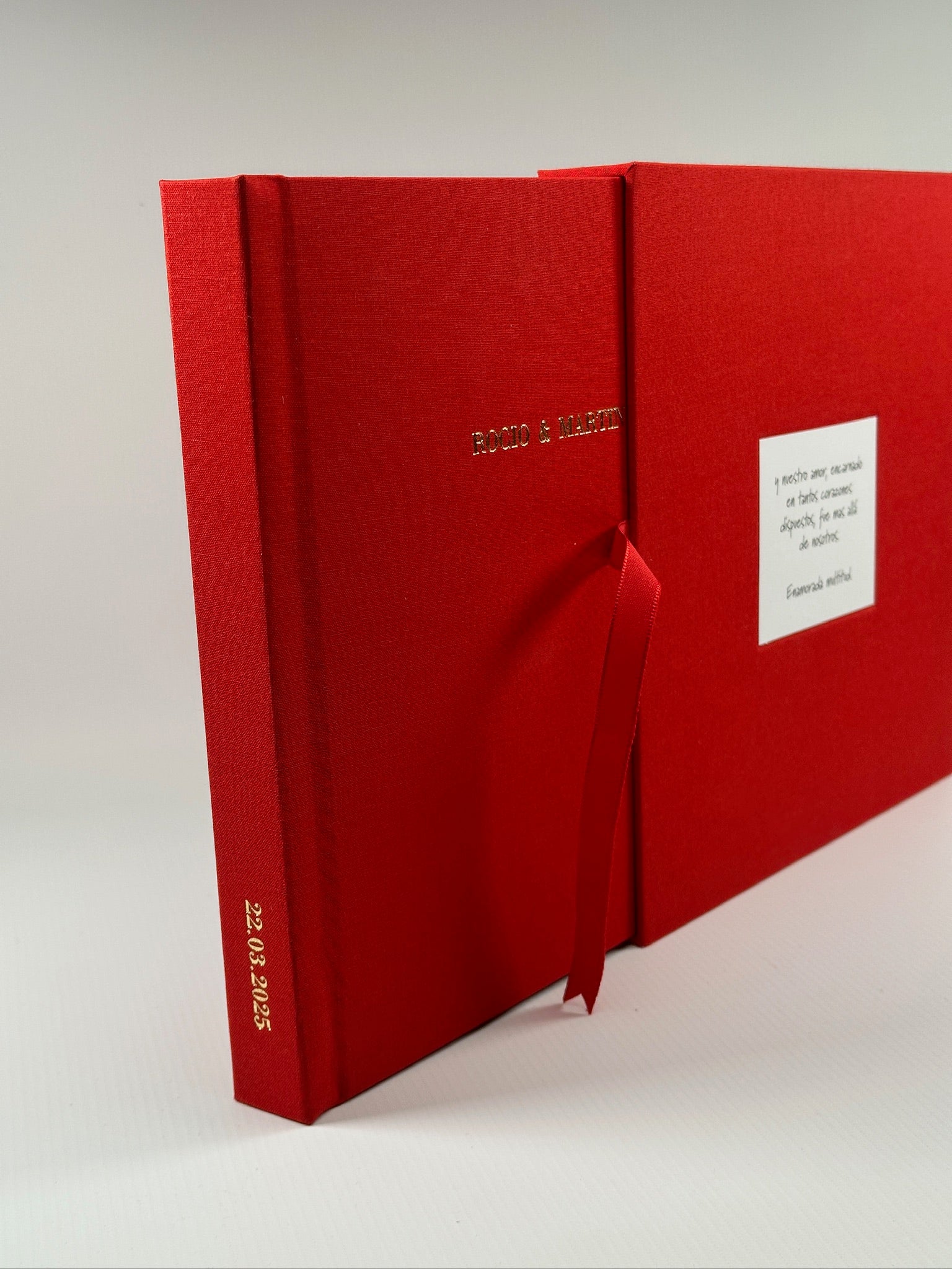 Vista angular del álbum rojo junto a su caja, nombres grabados y fecha al pie del lomo