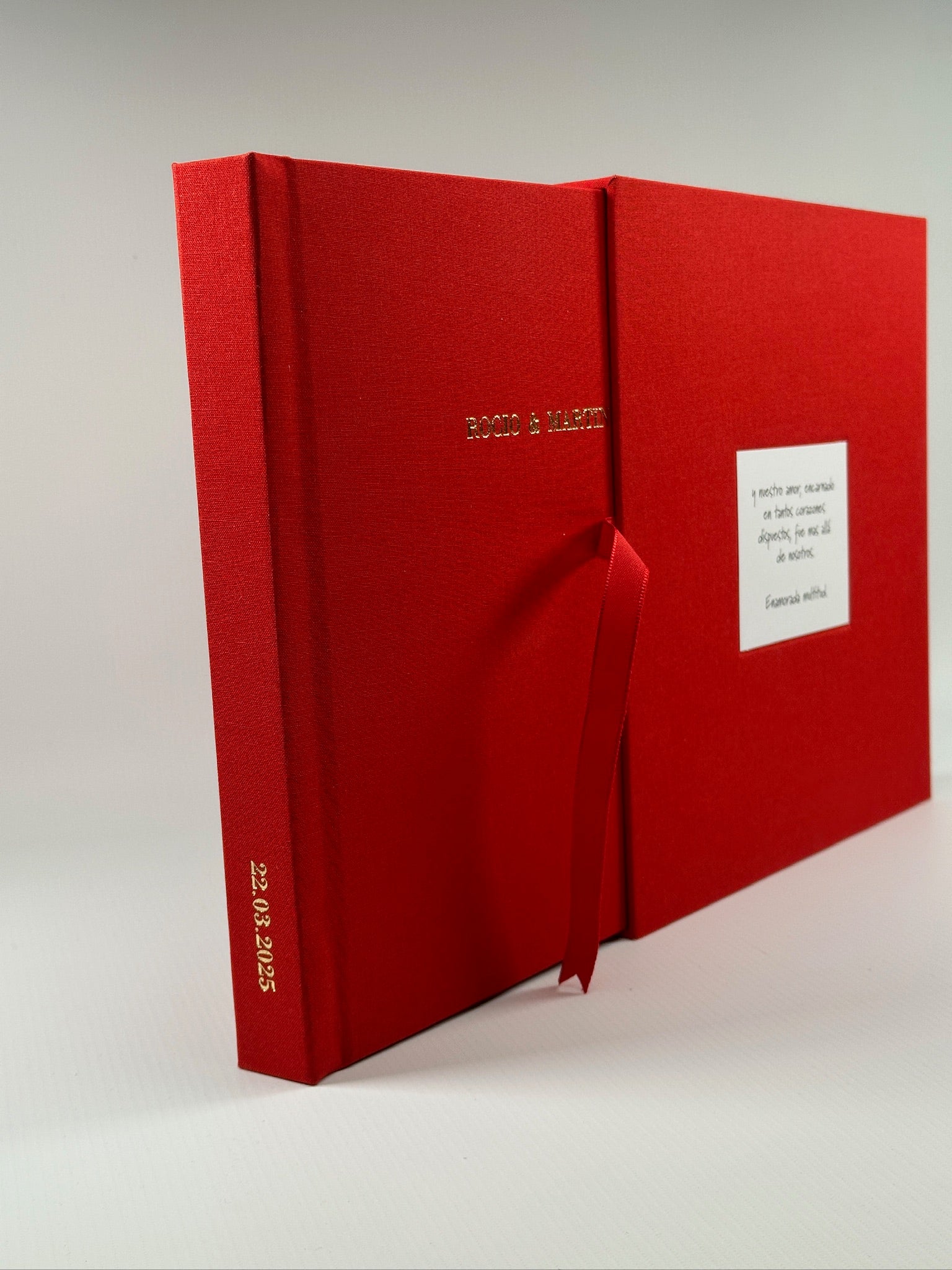 Fotolibro y estuche de lino rojo abiertos en abanico, con nombres en dorado y dedicatoria