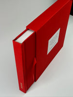 Fotolibro rojo asomando del estuche, mostrando el sistema de cinta para deslizar el álbum