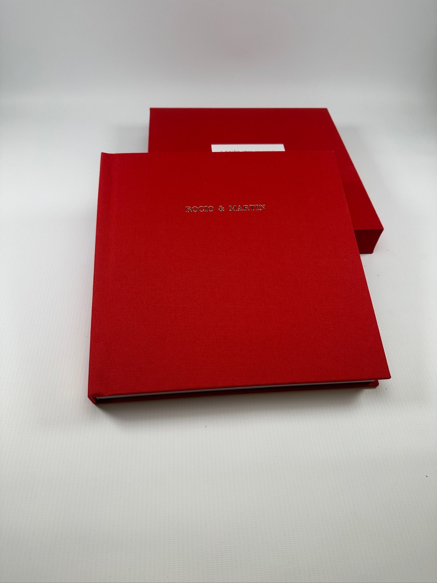 Fotolibro de tapa de lino rojo con nombres en dorado, apoyado sobre su estuche a juego