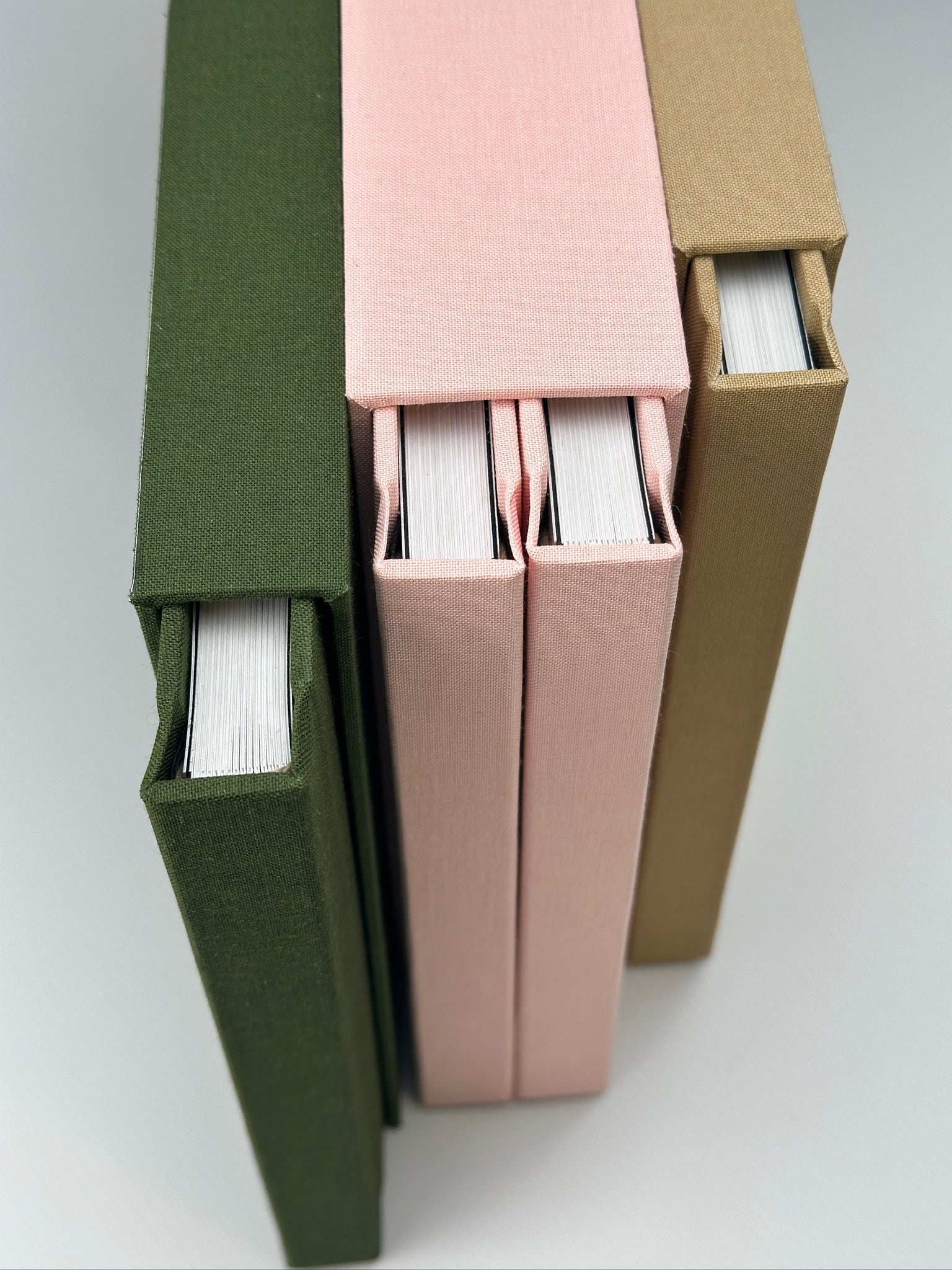 Detalle de estuches de lino verde, rosa y camel con los fotolibros de hojas gruesas asomando