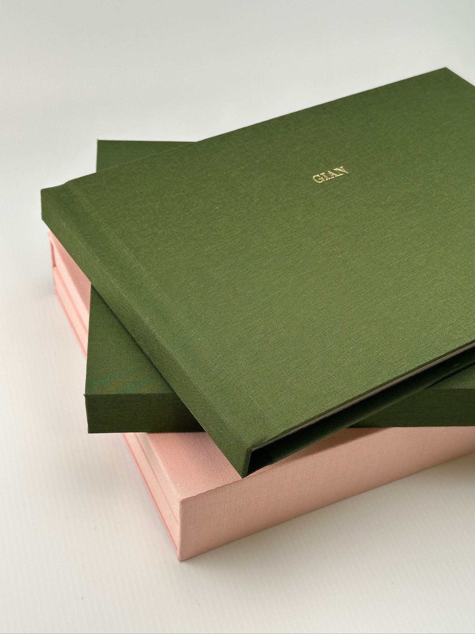 Estuches de lino camel apilados con uno de tono rosa intercalado, vistos de frente