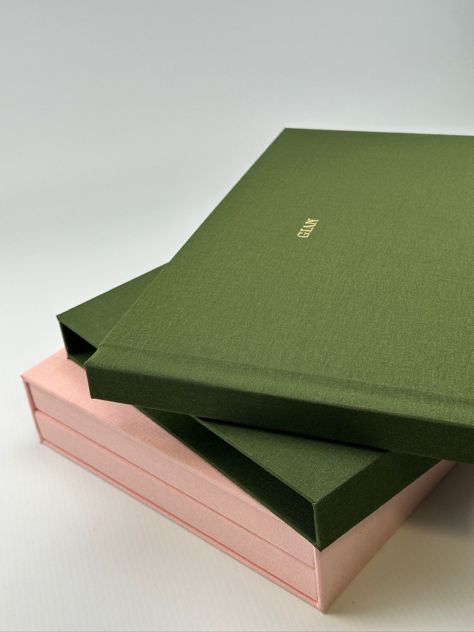 Detalle de varios estuches de lino camel apilados, con un fotolibro de canto rosa al medio