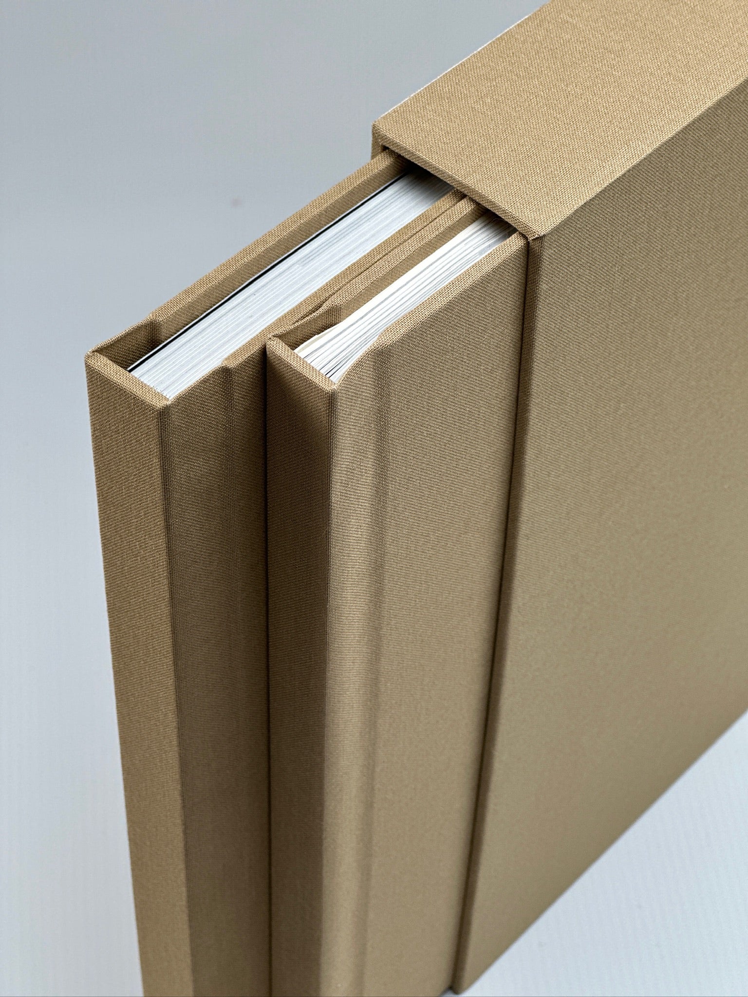 Dos fotolibros apaisados de lino camel adelante de su caja a juego, con nombre en dorado