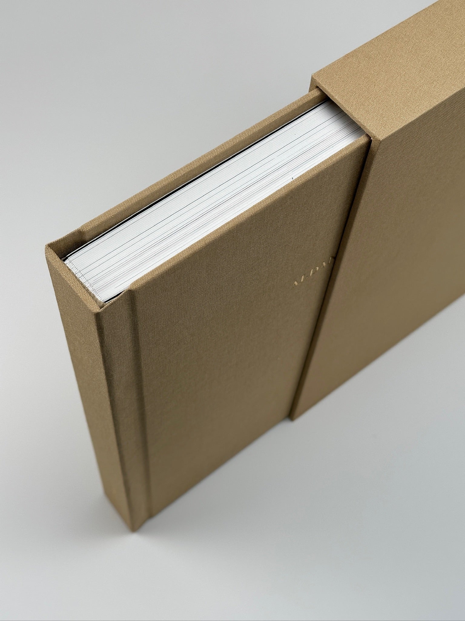 Dos fotolibros apaisados de lino camel apilados sobre su estuche, con nombres en dorado