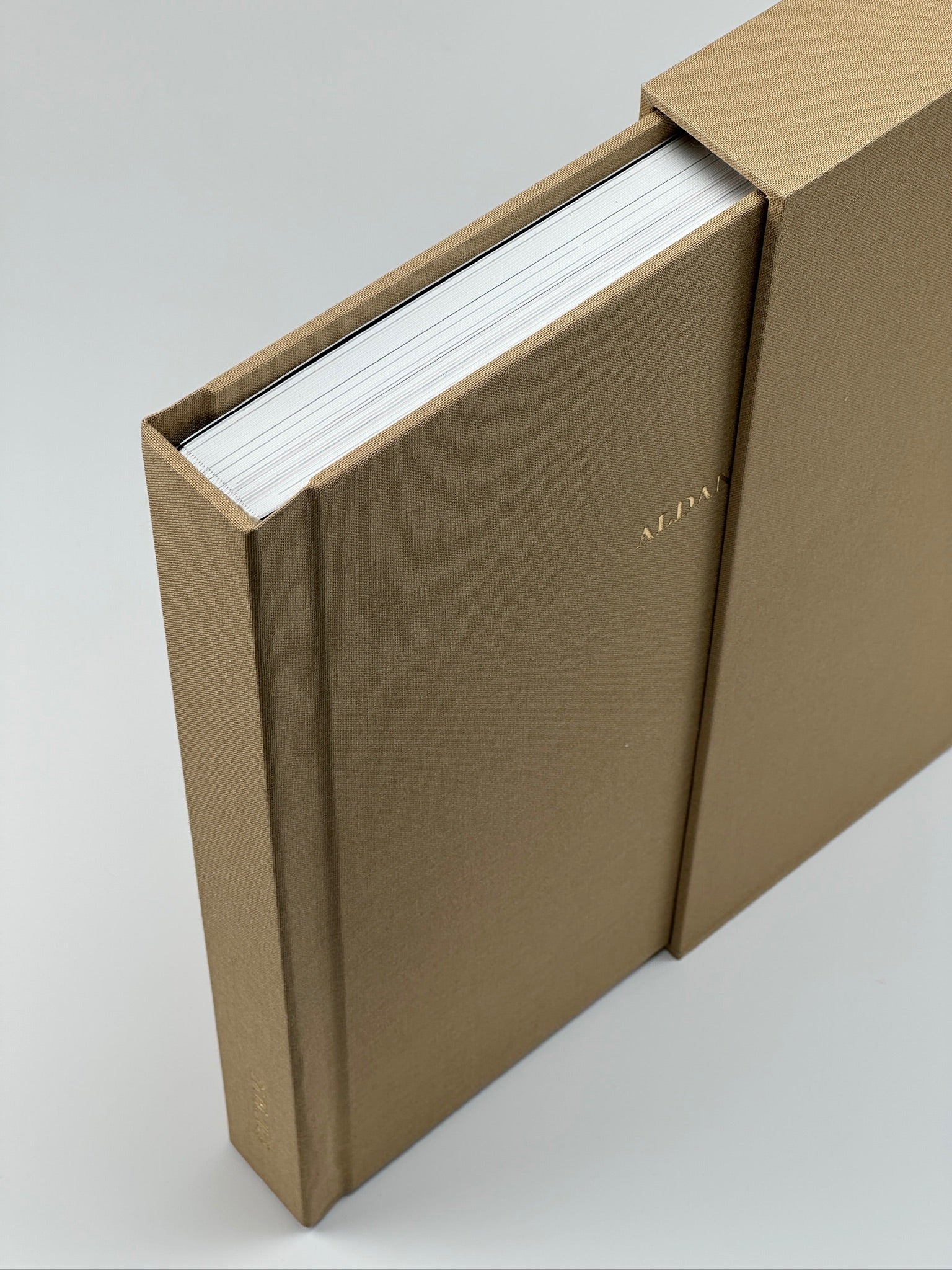Estuche de lino camel con el fotolibro a juego deslizándose hacia afuera, nombre en dorado