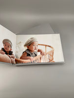 Fotolibro de bebé abierto a doble página, retrato de un nene con boina en una cuna de mimbre
