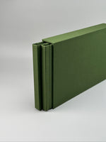 Estuche apaisado de lino verde oliva de canto, con el fotolibro entreabierto en el interior