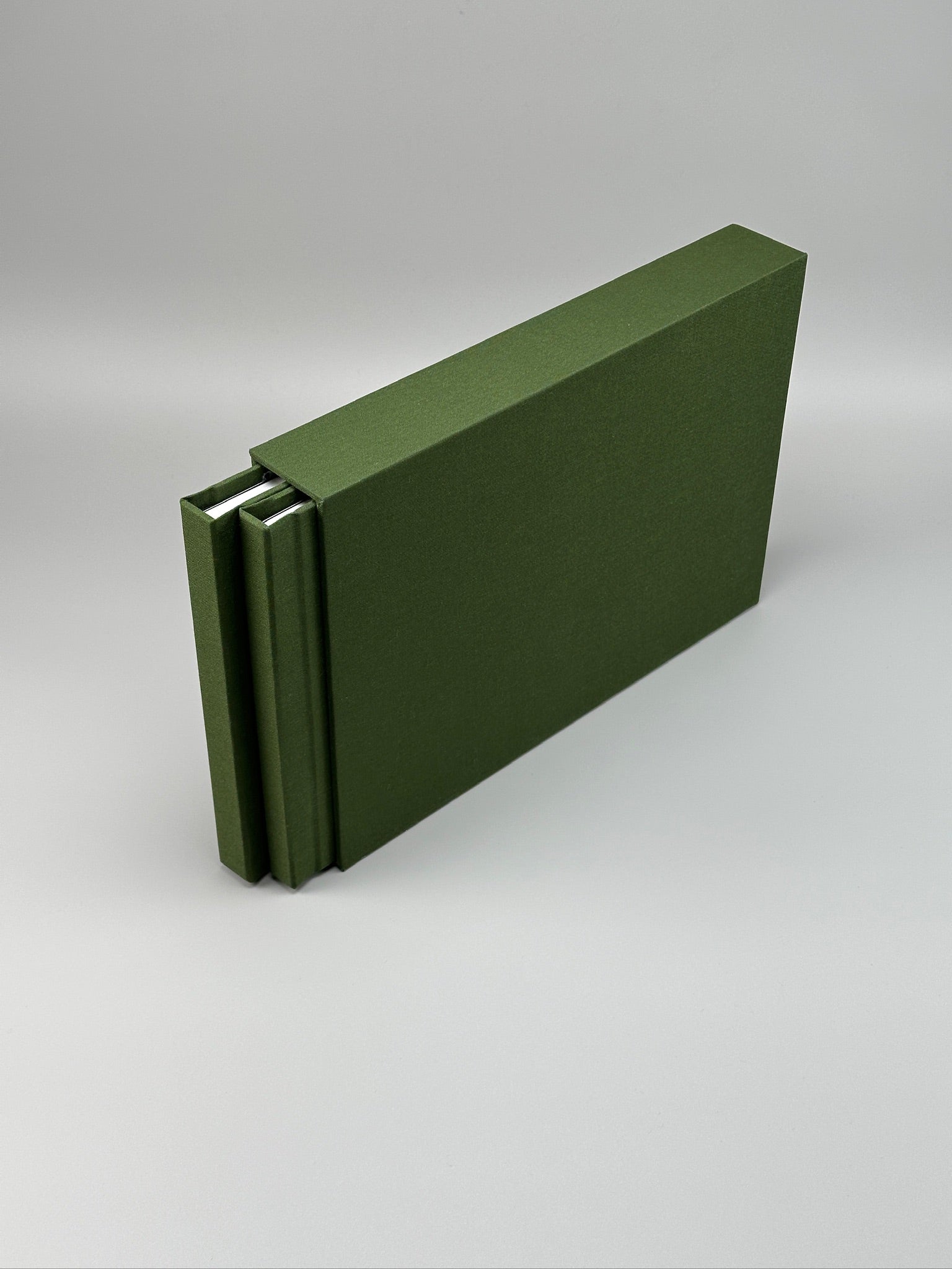 Estuche apaisado de lino verde oliva con el álbum a juego asomando por un costado