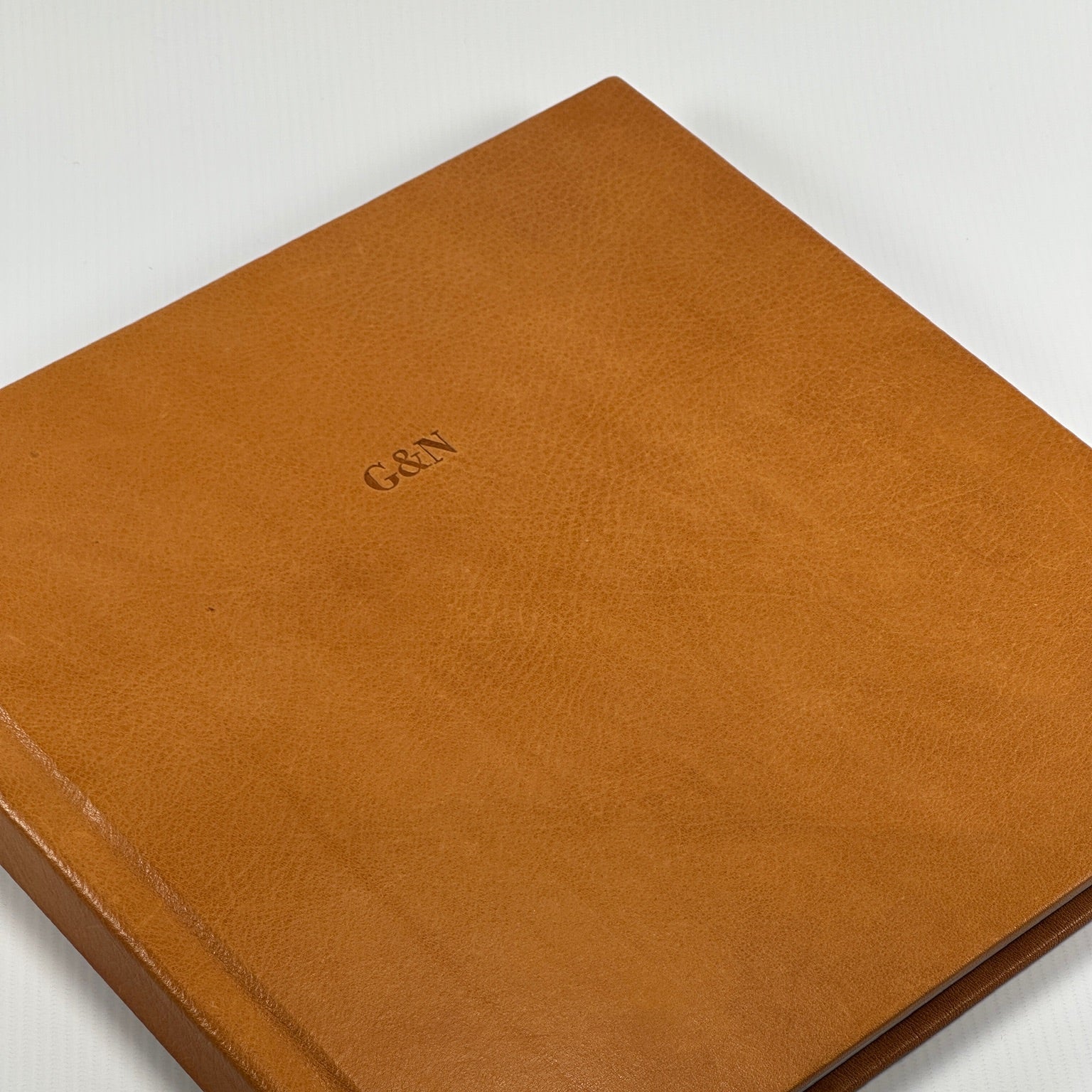 Tapa de cuero natural color cognac en ángulo con las iniciales G&N grabadas y textura del grano a la vista