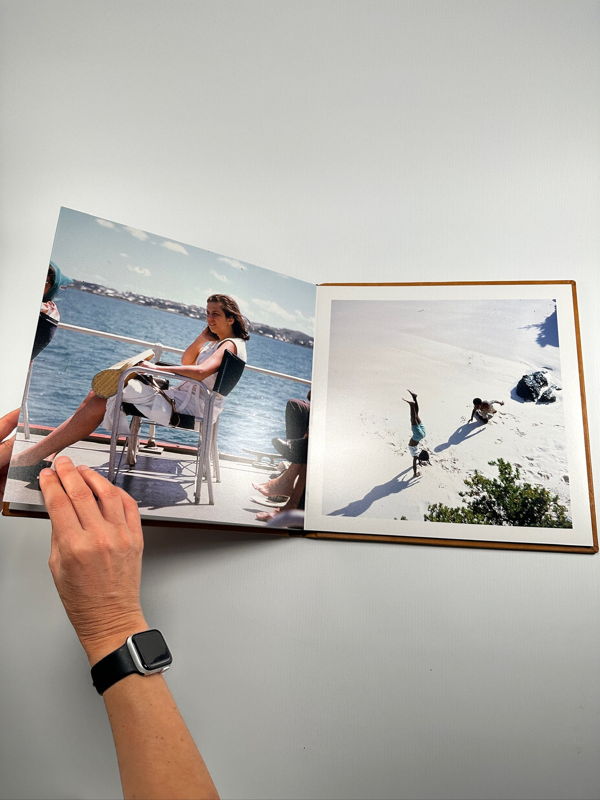 Fotolibro de cuero abierto a doble página mostrando fotos reales de un viaje a la playa, con mujer en un barco y chicos en la arena