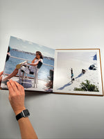 Fotolibro de cuero abierto a doble página mostrando fotos reales de un viaje a la playa, con mujer en un barco y chicos en la arena